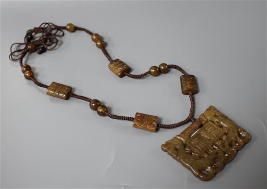 A Chinese hardstone necklace, with carved and inscribed plaque and brown fabric strung beads, plaque 6 x 4.5cm, rectangular beads 2cm a